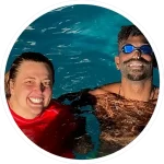 swimming teacher and adult swimmer bobbing in swimming pool and smiling at camera