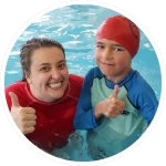 swimming teacher and young boy in pool smiling and showing thumbs-up