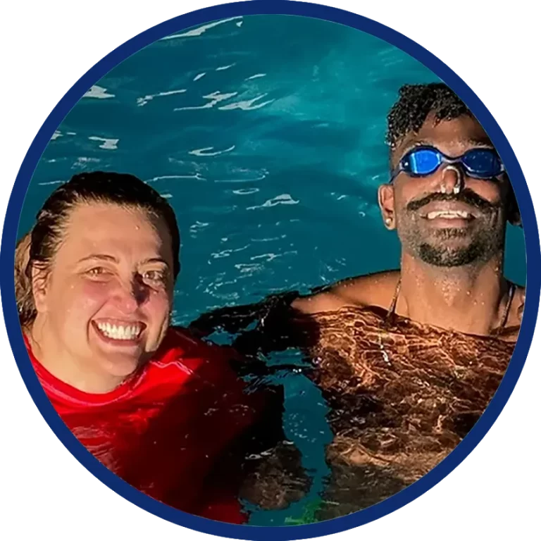 swimming teacher and adult swimmer bobbing in swimming pool and smiling at camera