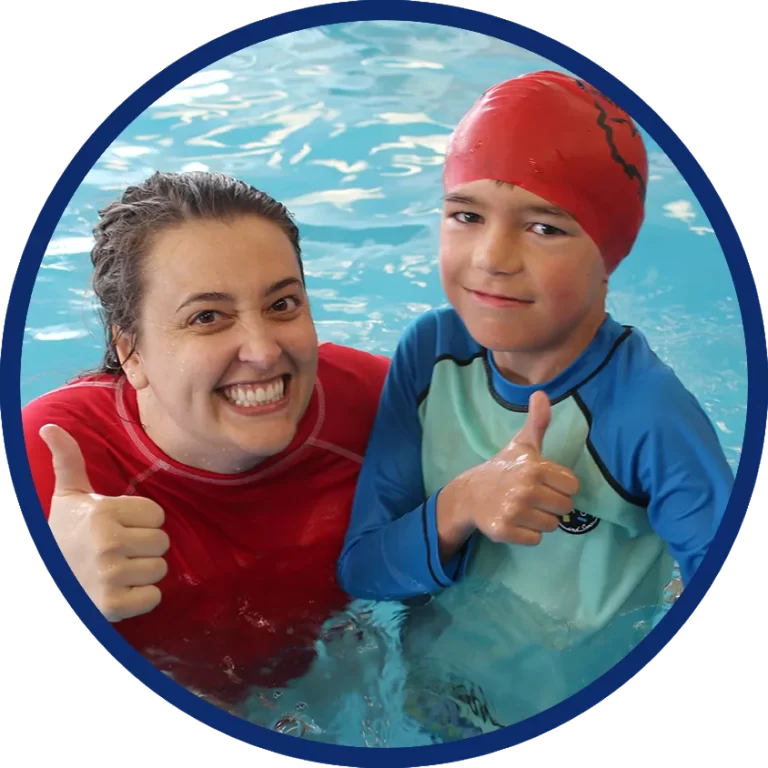 Private swimming lesson teacher and young boy in pool smiling and showing thumbs-up